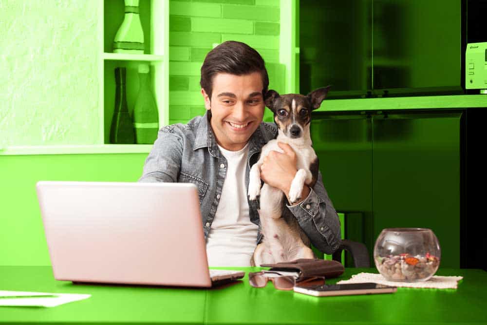 man smiling in front of his laptop holding his dog