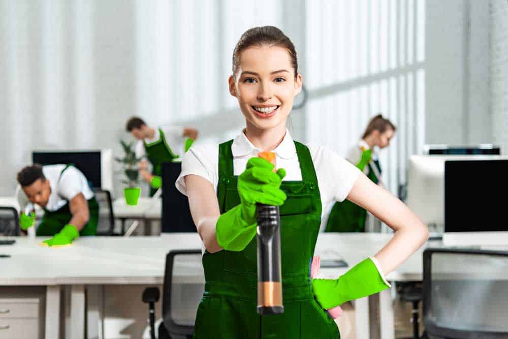 NRE Cleaning service done by a woman holding a spray wearing a green apron