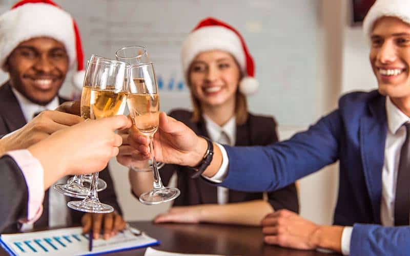 Employees wearing Santa hats raise a toast with their champagne glass flutes at the office Christmas party.