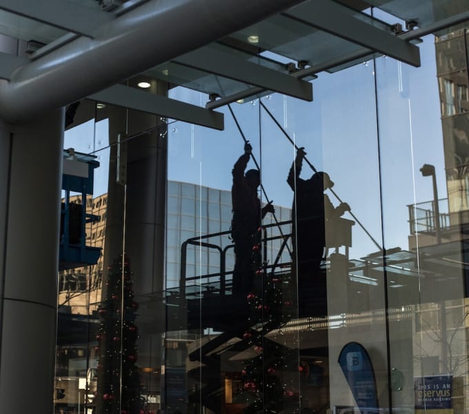 Reflection of commercial window cleaners cleaning the glass on the exterior of a building.