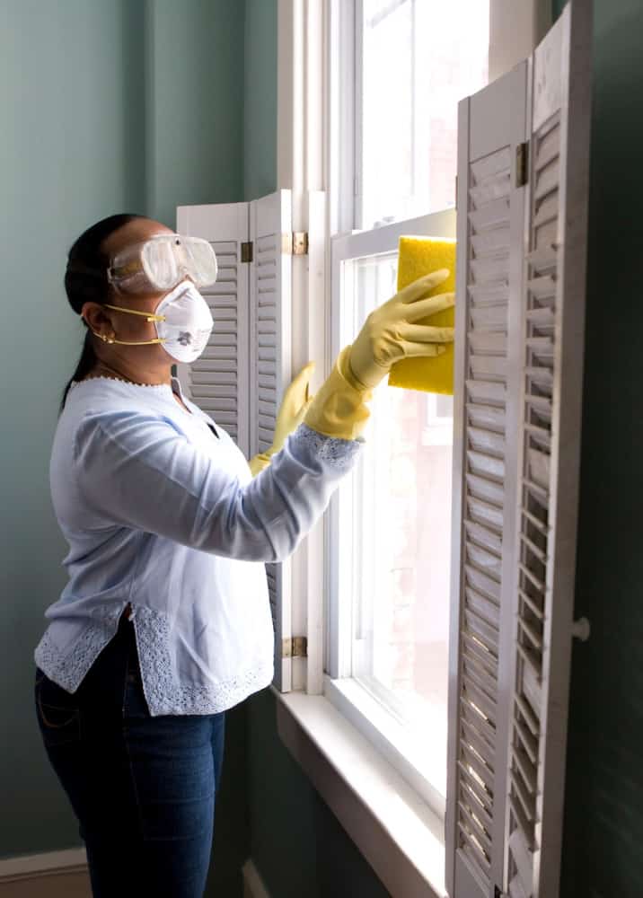 woman in mask, gloves, and goggles cleaning the glass window