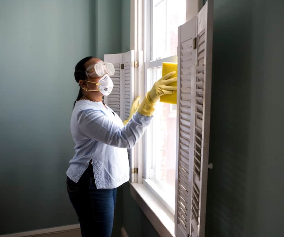 Professional cleaner wearing goggles and a mask, cleaning around a window frame